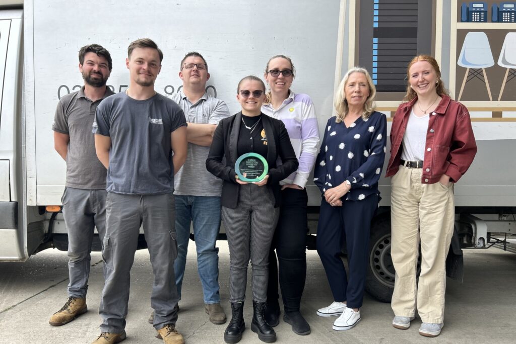 Seven people standing in front of a white truck, one holding a green circular award plaque